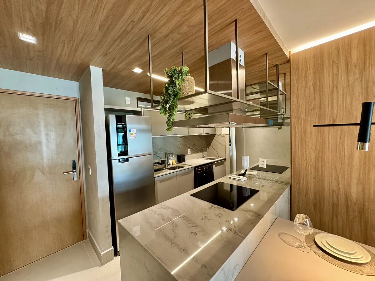 Cozinha completa e integrada com bancada e front\u00e3o em m\u00e1rmore, marcenaria em madeira e coifa central.