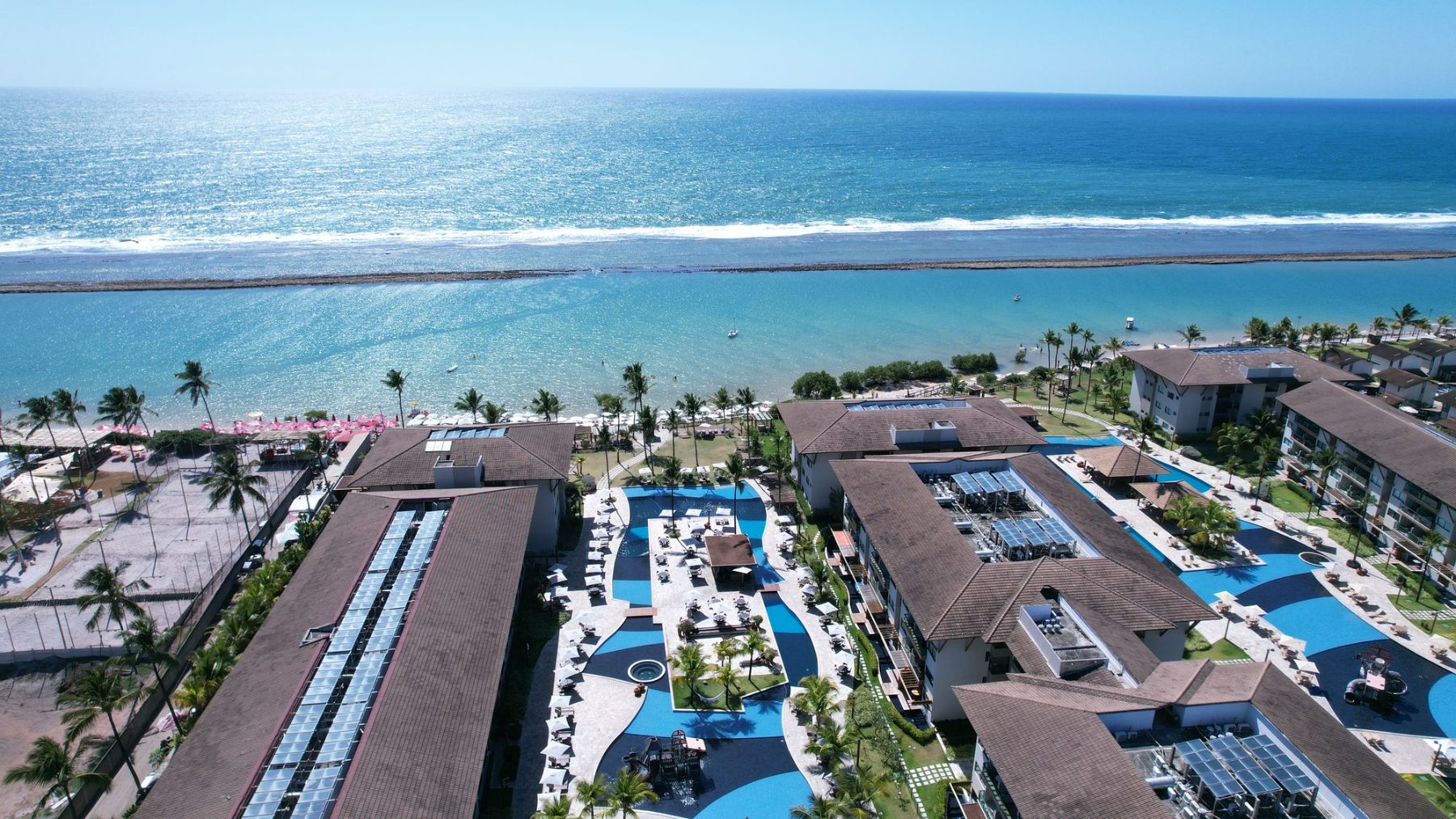 Samoa Beach Resort visto do alto: piscinas em curva entre os blocos, a faixa de coqueiros e a piscina natural de Muro Alto protegida pelo recife.