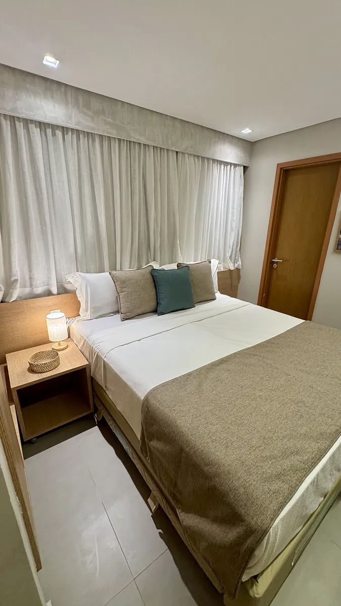 Quarto de casal com colcha bege e cortinas de linho.